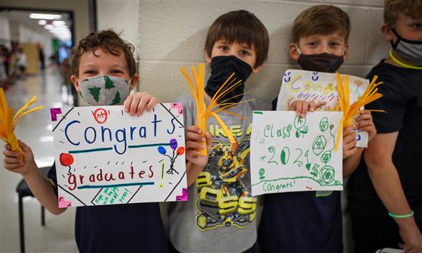 Students hold up signs for graduating seniors